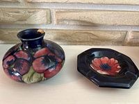 Photo showing both the Moorcroft vase and the ashtray side by side on a light-colored surface against a brick background, visible chip on vase rim.