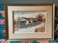 Full view of the framed oil painting showing a barn by water and a dirt path, in wood frame and fabric mat.