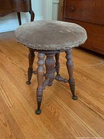 Side view of the vintage piano stool showing turned wooden legs with detailed carvings and aged fabric seat.