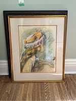 Framed print showing a side profile of a woman wearing a hat, light pastel colors, wooden frame with gold inner trim.