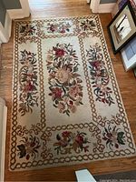 Full view of the hooked rug laid out on a hardwood floor showing floral design and border.