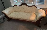 Front view of cream-colored settee with floral upholstery and ornate carved wood frame, showing detailed scrollwork and floral motifs on wooden accents. Matching decorative cushion included.