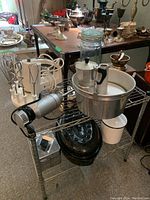 Metal shelving unit with small kitchen appliances and kitchenware displayed including mixers, espresso maker, cake pan, coffee grinder, and other items.