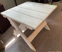 Side view of white painted wooden side table showing flat plank top and X-shaped legs folded out for use.