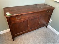 Wood sidebar angled view showing beveled top, partitioned drawer front, and two lower cabinet doors with handles and keyholes. Dark reddish-brown finish with some surface flaws.