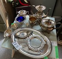 Full view of silver-plated coffee and tea set with two pots, sugar bowl, creamer, bowls, divided dish, and large serving platter on table.