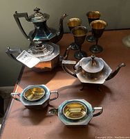 Full view of the silver plated tea and coffee set with copper wine cups on a brown surface