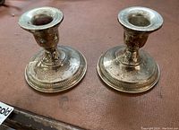 Two sterling silver weighted candle holders on a brown surface showing tarnish.