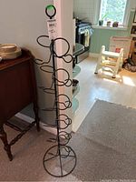 Photo of the entire black metal vertical wine rack standing on the floor next to a wooden table and kitchen area.