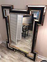 Front view of Art Deco style rectangular wall mirror with black and gold geometric frame hung on a wall.