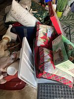 Photo showing assorted Christmas decorative pillows, a storage bin, sealed garland box, and additional holiday decor items arranged closely.