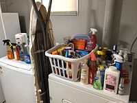 View of laundry basket filled with cleaning products, ironing board, and laundry rack in background
