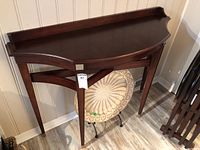 Full view of wooden half-moon console table with tapered legs and curved backsplash.