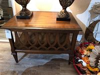 Front view of the wooden end table with lamps on top, highlighting top surface and decorative side panel.