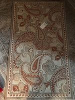 Top down image of burnt orange and beige floor rug with paisley and floral patterns, bordered design
