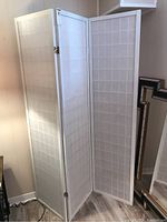 Three-panel white folding room divider made of wood with rice paper inserts, standing upright in a corner.