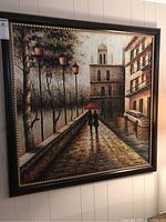 Full view of large framed painting showing rainy street scene with two people walking under red umbrella, buildings, car, and street lamps.