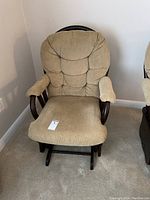 Front view of beige upholstered glider rocker chair showing tufted backrest and padded arms