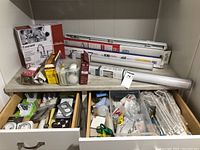 Shelves and drawers showing packaged and loose light bulbs, blinds stored on top and various hardware items in open drawers.