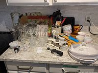 Full shot of the kitchen countertop displaying all items including glassware, mugs, bowls, utensils, and serving dishes as in the mixed lot