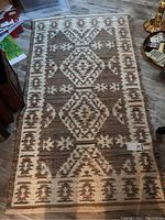 Full view of rag-style area rug on floor with geometric diamond patterns and earth tone colors.