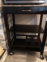 Full view of the rolling utility cart showing three levels of espresso wood shelves including the bottom shelf with wine bottle cutouts and caster wheels.