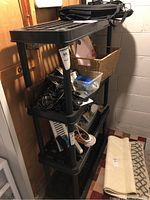 Side view of black plastic shelving unit with items on shelves for scale, showing grid pattern and vertical support columns.