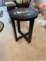 Side angle photo showing the round wooden side table with dark finish and glass inset top, four legs, and cross supports.