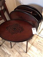 Set of four oval wooden TV tables with rounded edges and ornate black patterns on top, stacked and arranged showing design and shape.