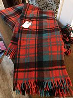 Photo of one folded wool blanket showing its red, green, and black plaid pattern with fringed edges.