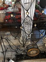 Photo showing black metal wall decor with geometric elongated oval shapes accented with gold spheres, clock partially visible, and candle votive holder on floor.