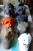 View of nine assorted ball caps from front and top angles, showing logos and colors, arranged on white surface
