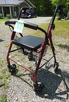 Front view of red Bios Diagnostics walker showing leather seat, hand brakes, front basket, and four wheels on gravel.