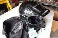 Left side angled view of glossy black full-face Polaris helmet resting on the black branded helmet bag, showing visor and vents.
