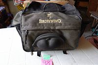 Exterior view of brown/olive canvas Browning tackle bag showing front molded compartment and Browning logo embroidered in gold.