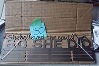 Brown metal wall hanging with motivational phrase and medal display slots, placed on cardboard with a lot sticker