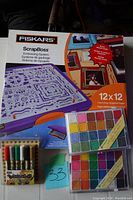 Fiskars ScrapBoss embossing system box featuring 12x12 embossing paper and a set of Terra cotta craft markers (6 colors). Also visible is one chalk set in a palette box.