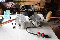 Full view of deep fryer burner with two perforated fryer baskets attached and gas hose with regulator.