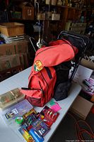 Full view of red Bass Pro backpack/stool combo with fishing rods attached and assorted tackle on table