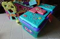 Photo showing decorated turquoise and purple storage container with compartments on its lid, in front of the green and purple tree house playset.