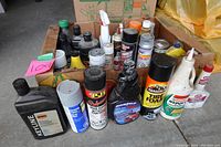 Box with various used automotive cleaners and fluids, showing different brands and product types such as brake cleaner, tire foam, and engine treatments.