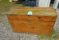 Front view of an old wooden chest placed outdoors showing the full chest with weathered wood and metal hardware.