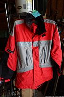 Front view of Polaris riding jacket with red, gray, black panels and reflective silver striping across chest and sleeves. Two zippered pockets on front and zippered ventilation fields visible.