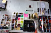 Top-down view of four tackle boxes with various fishing lures, soft plastic worms, hooks, swivels, and fishing line spools visible.