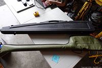 Two gun cases side by side on a white table: a black hard case and a green soft case.