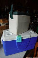 Two Coleman coolers stacked, large blue and white cooler on bottom, smaller white and green cooler on top. Used condition.