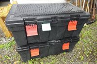 Two black plastic storage totes stacked outdoors, showing red locking latches and textured lid.