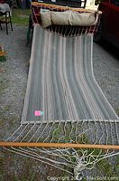 Full view of green and beige striped canvas hammock laid out on the ground showing fabric and top wooden spreader bar with suspension ropes.