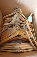 Set of wooden hangers in a box, showing metal hooks and natural wood finish with some branding visible