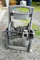Front view of gray Yardworks hose reel cart with hose wrapped around the metal axle, placed on gravel ground outside. Shows cart's wheels, handle, and hose.